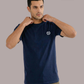 Mann im dunkelblauen T-Shirt mit weißem Lorbeerkranz-Logo, greift an den Kragen, dazu khakifarbene Cargohose.