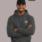 Lächelnder Mann mit Cap im dunkelgrauen Hoodie mit Logo: Ein Lorbeerkranz umschließt ein kreisförmiges, gezacktes Symbol.