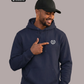 Mann mit Cap im blauen Hoodie, zeigt auf Logo: Ein Lorbeerkranz umschließt ein kreisförmiges, gezacktes Symbol.