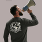 Rückansicht eines Mannes im dunkelgrauen Sweatshirt mit großem „Matchday“-Rückenprint, der in ein Megafon ruft.