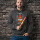 Ein Mann vor einer Backsteinwand trägt einen dunkelgrauen Hoodie mit dem Comic-Print einer Pyro-Figur vor einer Größenskala und Schriftzügen, während er eine rote Fackel in der Hand hält