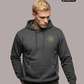 Ein Mann trägt einen dunkelgrauen Kapuzenpullover mit einem kreisförmigen, gelb-grauen „STANDHAFT“-Logo samt kleiner Krone auf der linken Brust.