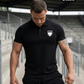 Ein Mann mit gesenktem Blick auf einer Stadiontribüne trägt ein schwarzes Poloshirt mit einem weißen Wappen-Logo samt Adlergrafik und „STANDHAFT“-Schriftzug auf der linken Brust.