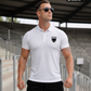 Ein Mann mit Sonnenbrille auf einer Stadiontribüne trägt ein weißes Poloshirt mit einem schwarzen Wappen-Logo samt Adlergrafik und „STANDHAFT“-Schriftzug auf der linken Brust.