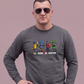Mann mit Sonnenbrille trägt grauen Sweatshirt-Pullover mit „All Colors Are Beautiful“-Grafikprint vor beigem Hintergrund.