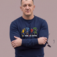 Mann mit verschränkten Armen trägt dunkelblauen Sweatshirt-Pullover mit „All Colors Are Beautiful“-Print vor grauem Hintergrund.