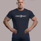 Mann in blauem Navyblue T-Shirt mit weißem Aufdruck „STAND HAFT“ und Adler-Logo steht mit eingestemmten Händen vor grauem Hintergrund. AI-generated.