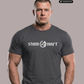 Mann in grauem T-Shirt mit weißem Aufdruck „STAND HAFT“ und Adler-Logo blickt ernst vor grauem Hintergrund. AI-generated.