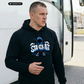 Ein Mann trägt einen schwarzen Hoodie mit einem blauen Comic-Grafik-Print und dem Schriftzug „STANDHAFT“.