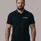 Bärtiger Mann im schwarzen Poloshirt mit weißem Brustaufdruck „Standhaft“, frontaler Blick, dazu Jeans.