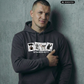 Kurzhaariger Mann im dunkelgrauen Hoodie mit dem Aufdruck „STANDHAFT“ und vier Motivkarten vor Betonwand.