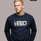 Blonder Mann in dunkelblauem Pullover mit der Aufschrift „STANDHAFT“ und vier Motivkarten, dazu blaue Jeans.