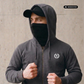 Mann mit Cap und Gesichtsmaske in dunkelgrauer Zipper-Jacke mit Lorbeerkranz-Logo, Blick nach links gerichtet.