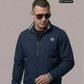 Mann mit Sonnenbrille in dunkelblauer Bomberjacke mit Lorbeerkranz-Logo und hellen Streifen an Kragen und Bündchen.