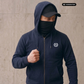 Mann mit Cap und Gesichtsmaske in dunkelblauer Zipper-Jacke mit Lorbeerkranz-Logo, Blick nach rechts gerichtet.