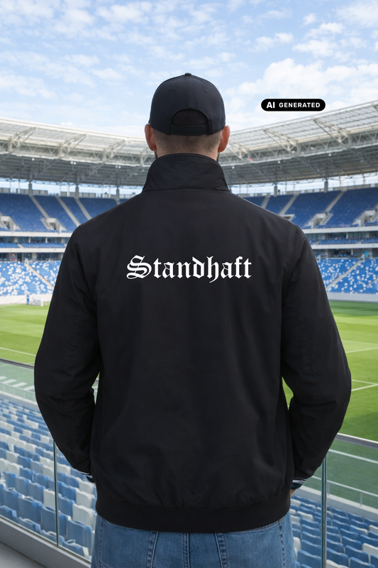 Ein Mann von hinten in einer schwarzen Bomberjacke mit weißem „Standhaft“-Schriftzug im altdeutschen Stil auf dem Rücken.