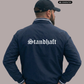 Ein Mann von hinten in einer dunkelblauen Bomberjacke mit weißem „Standhaft“-Schriftzug im altdeutschen Stil auf dem Rücken.