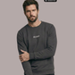 Ein Mann trägt einen dunkelgrauen Pullover mit einem kleinen, weißen „Standhaft“-Schriftzug auf der Brust.