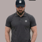 Bärtiger Mann mit Cap im dunkelgrauen Poloshirt mit Lorbeerkranz-Logo, Blick nach unten gerichtet.