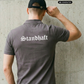 Ein Mann von hinten in einem grauen Poloshirt mit weißem „Standhaft“-Schriftzug im altdeutschen Stil auf dem Rücken.