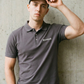 Ein Mann trägt ein graues Poloshirt mit einem kleinen, weißen „Standhaft“-Schriftzug auf der linken Brust.
