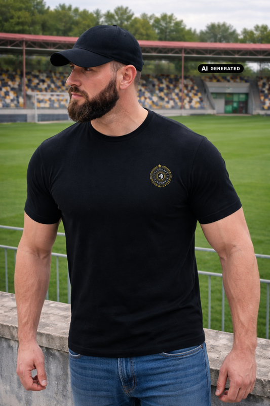 Ein Mann mit schwarzer Basecap im Stadion trägt ein schwarzes T-Shirt mit einem kreisförmigen, gelb-schwarzen „STANDHAFT“-Logo samt kleiner Krone auf der linken Brust.