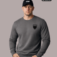 Ein Mann mit schwarzer „STHF“-Basecap und den Händen in den Taschen trägt einen dunkelgrauen Pullover mit einem schwarzen Wappen-Logo samt Adlergrafik und „STANDHAFT“-Schriftzug auf der linken Brust.