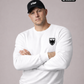 Ein Mann mit schwarzer „STHF“-Basecap und verschränkten Armen trägt einen weißen Pullover mit einem schwarzen Wappen-Logo samt Adlergrafik und „STANDHAFT“-Schriftzug auf der linken Brust.