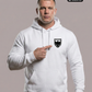 Ein Mann, der mit dem Finger auf die Brust zeigt, trägt einen weißen Hoodie mit einem schwarzen Wappen-Logo samt Adlergrafik und „STANDHAFT“-Schriftzug auf der linken Brust.