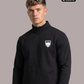 Ein Mann trägt eine schwarze Trainingsjacke mit Reißverschluss und einem weißen Wappen-Logo, das einen Adler und den Schriftzug „STANDHAFT“ zeigt, auf der linken Brust