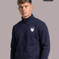Ein Mann trägt eine dunkelblaue Trainingsjacke mit Reißverschluss und einem weißen Wappen-Logo, das einen Adler und den Schriftzug „STANDHAFT“ zeigt, auf der linken Brust