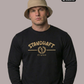 Ein Mann mit beigem Anglerhut trägt einen schwarzen Pullover mit goldenem „STANDHAFT“-Schriftzug und Lorbeerkranz-Logo auf der Brust.