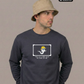 Ein Mann mit beigem Anglerhut trägt einen dunkelblauen Pullover mit einer Comic-Grafik auf der Brust.