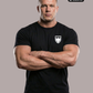 Ein Mann mit verschränkten Armen trägt ein schwarzes T-Shirt mit einem weißen Wappen-Logo samt Adlergrafik und „STANDHAFT“-Schriftzug auf der linken Brust.
