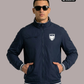 Ein Mann mit Sonnenbrille und den Händen in den Taschen trägt eine dunkelblaue Bomberjacke mit weiß-grauen Streifenbündchen und einem weißen Wappen-Logo samt Adlergrafik und „STANDHAFT“-Schriftzug auf der linken Brust.