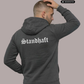 Ein Mann von hinten in einem dunkelgrauen Zip Hoodie mit weißem „Standhaft“-Schriftzug im altdeutschen Stil auf dem Rücken.
