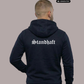 Ein Mann von hinten in einem dunkelblauen Zip-Hoodie mit weißem „Standhaft“-Schriftzug im altdeutschen Stil auf dem Rücken.