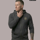 Ein Mann trägt eine dunkelgraue Zip-Jacke mit Kapuze und einem kreisförmigen, gelb-grauen „STANDHAFT“-Logo samt kleiner Krone auf der linken Brust.