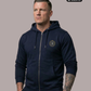 Ein Mann trägt eine dunkelblaue Zip-Jacke mit Kapuze und einem kreisförmigen, gelb-blauen „STANDHAFT“-Logo samt kleiner Krone auf der linken Brust.