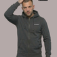 Ein Mann trägt eine dunkelgraue Zip-Jacke mit Kapuze und einem kleinen, weißen „Standhaft“-Schriftzug auf der linken Brust.
